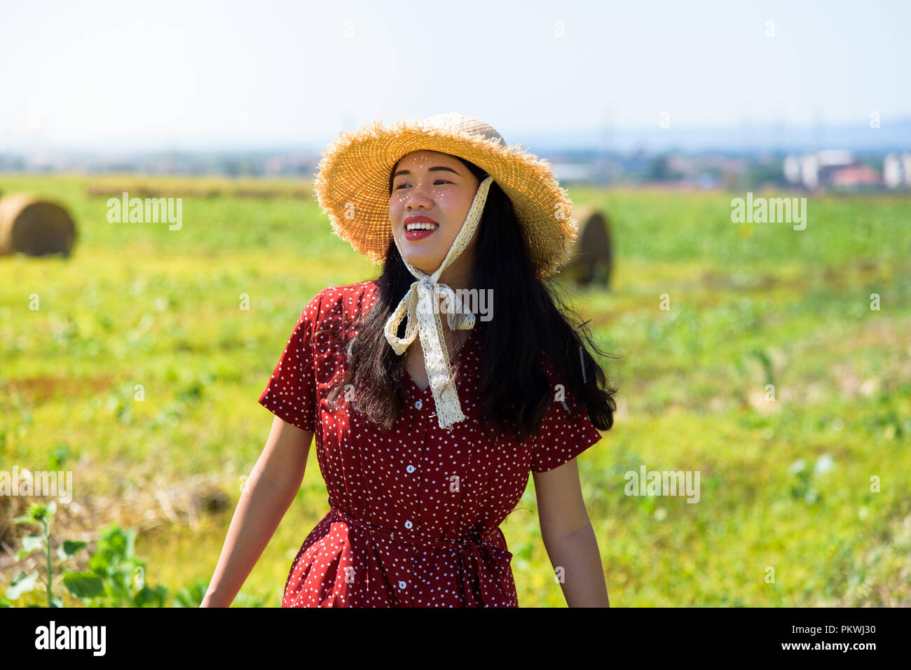 Asian girl relaxing outdoors in in a wheat field wearing red dress Stock Photo