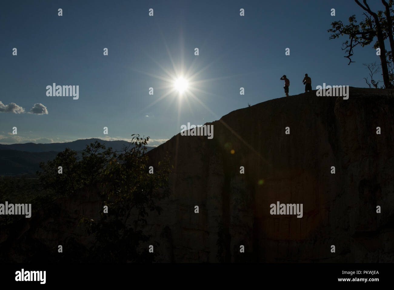 Silhouette of two men on a mountain peak with a sunburst above. Pai Canyon Thailand Stock Photo