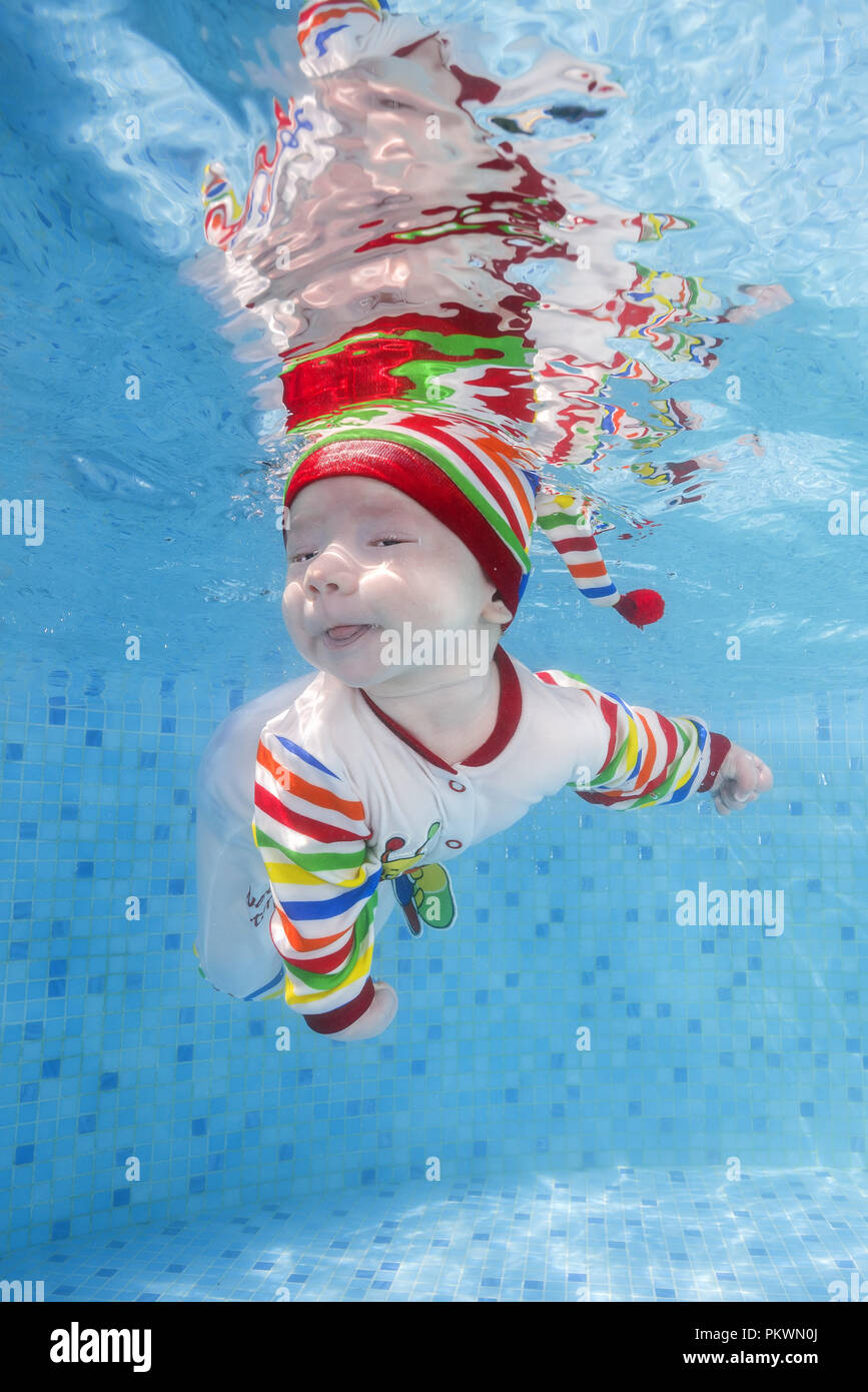 3 months boy in a bright striped swimming suit swims underwater in the pool Stock Photo