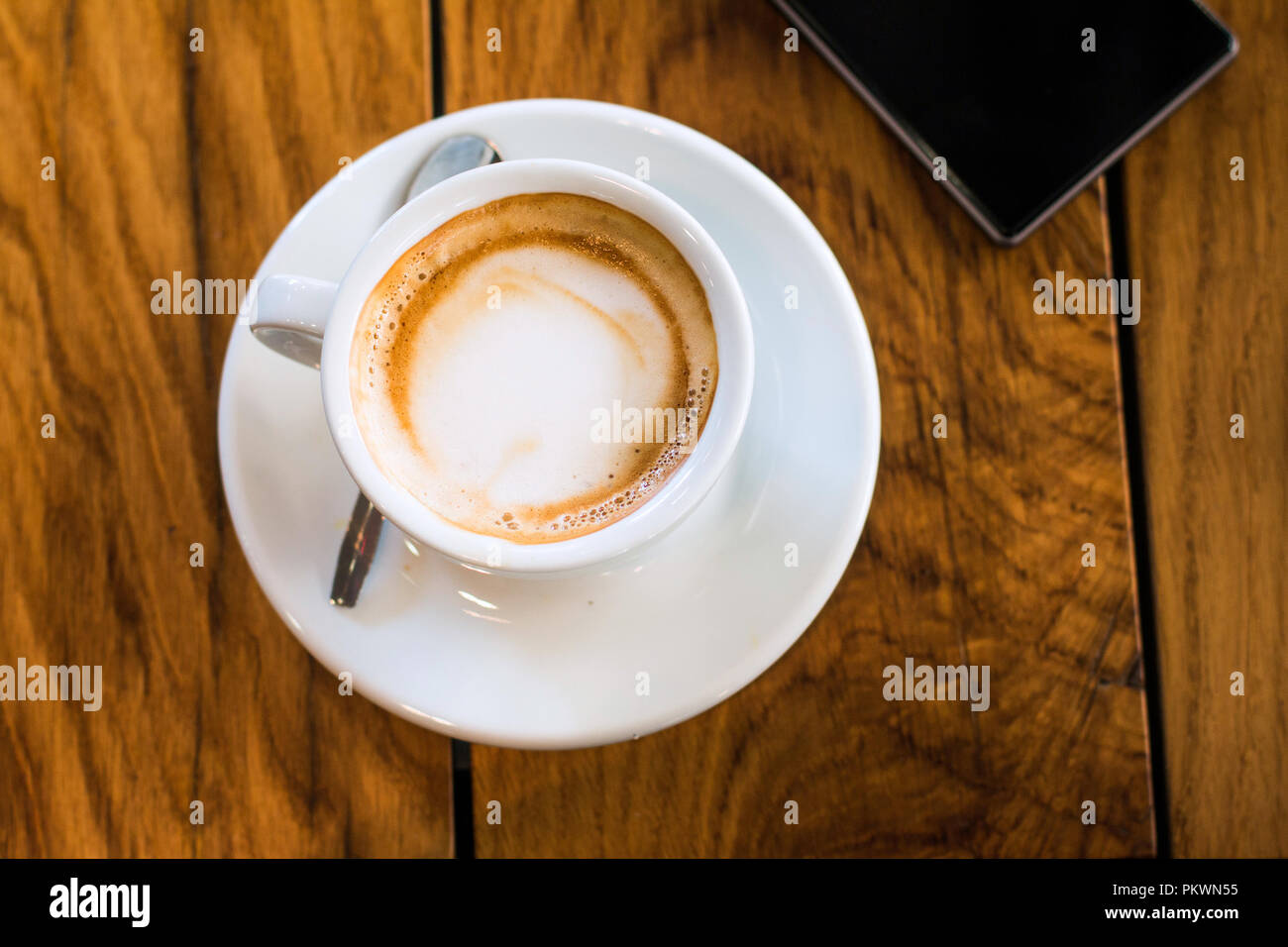A cup of coffee and smart phone on a woden table in cafe Stock Photo