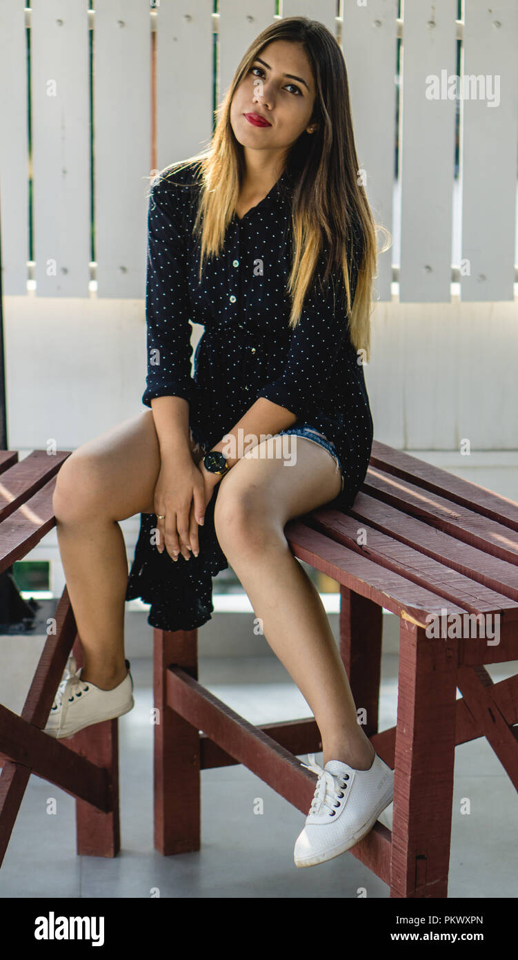 Girl posing for the camera while sitting on a wooden table in a balcony. Stock Photo