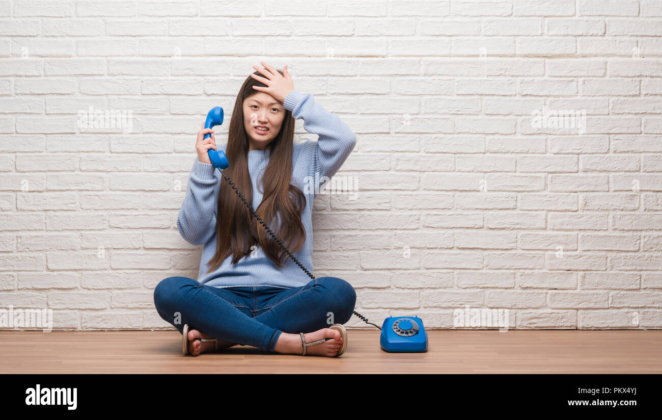 Young Chinese woman calling using vintage telephone stressed with hand on head, shocked with shame and surprise face, angry and frustrated. Fear and u Stock Photo