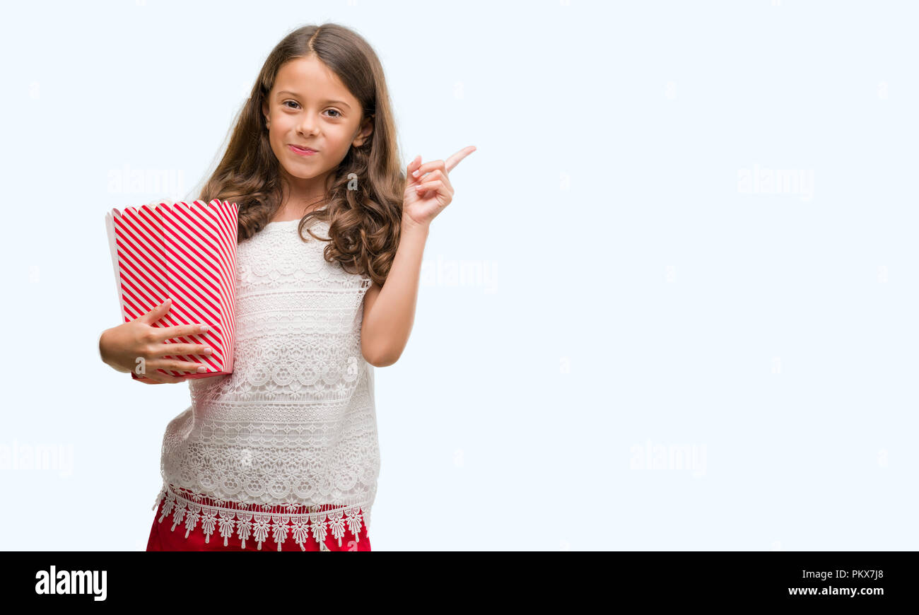 Brunette hispanic girl eating popcorn very happy pointing with hand and finger to the side Stock Photo