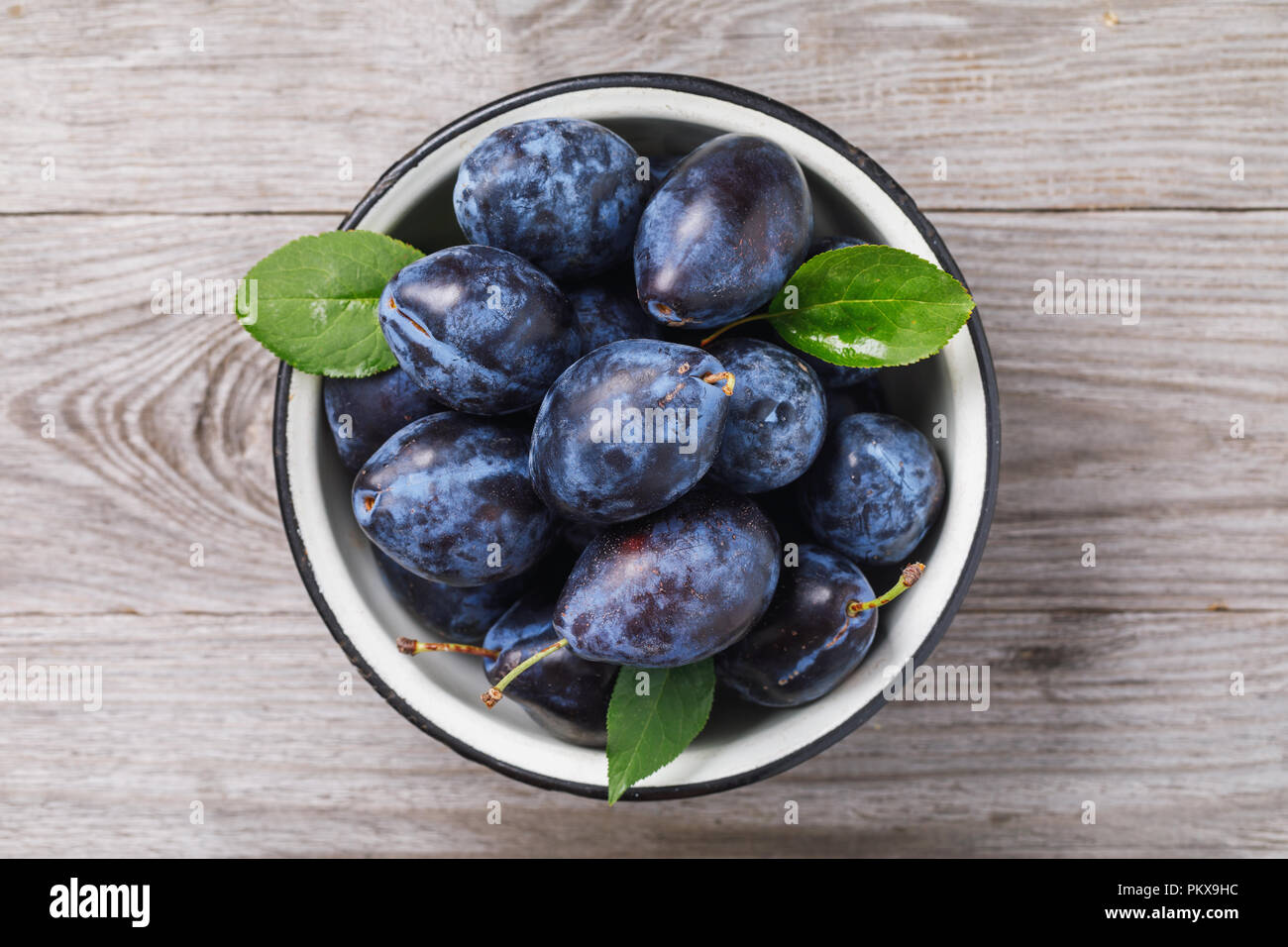 Top view of a bowl full of ripe prune fruit on a wooden table Stock Photo