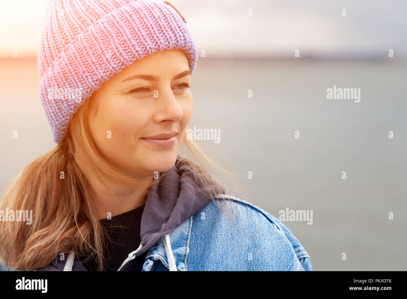 Closeup of happy beautiful young woman in blue knitted hat and denim coat, smiling, posing, outdoors on sunny autumn day. Stock Photo