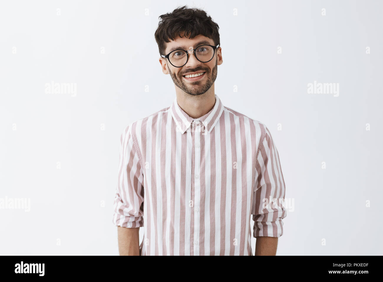 Emotive And Funny Cute Bearded Guy With Dark Stylish Hairstyle Tilting Head And Smiling With Polite Emotive And Funny Cute Bearded Guy With Dark Stylish Hairstyle Tilting Head And Smiling With Polite