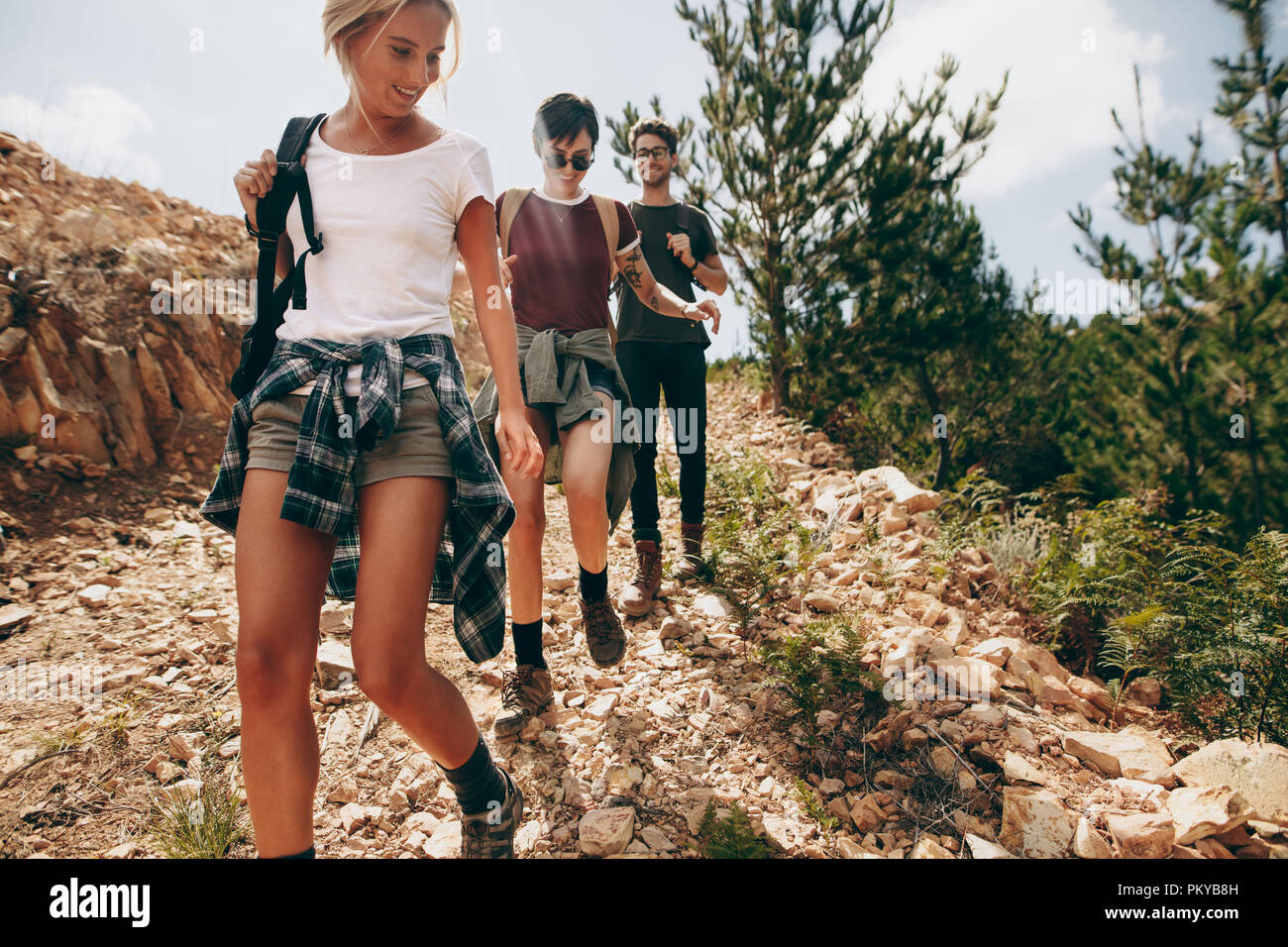 Friends hiking down a rugged hilly terrain. Man with two female friends walking on a rocky path in a country side location. Stock Photo