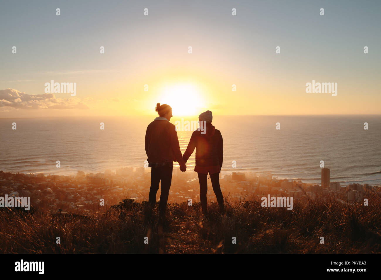 Silhouette of man and woman holding hands and standing on the mountain ...