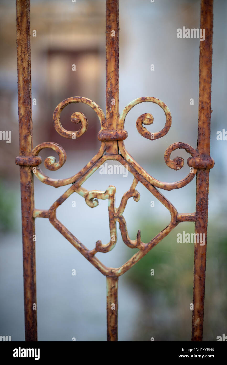 Old rusty iron gate with letter K, abandoned house in background Stock Photo