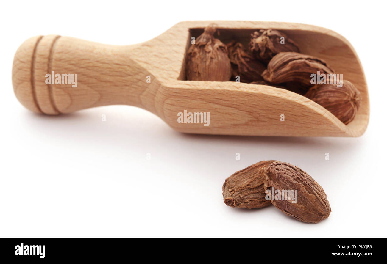 Black cardamom in wooden scoop over white background Stock Photo