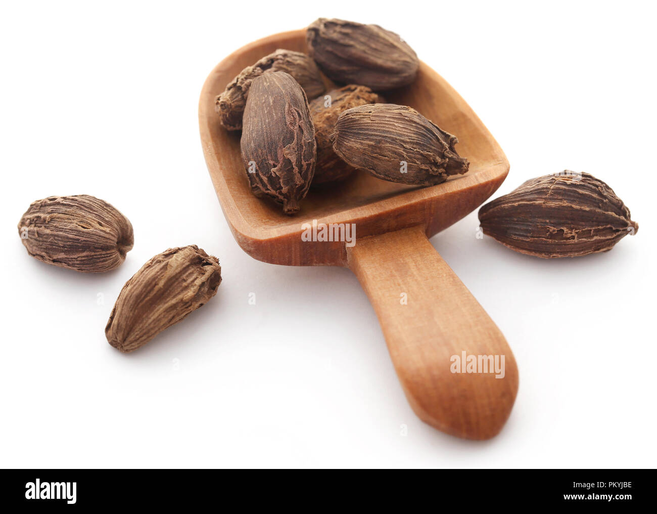 Black cardamom in wooden scoop over white background Stock Photo