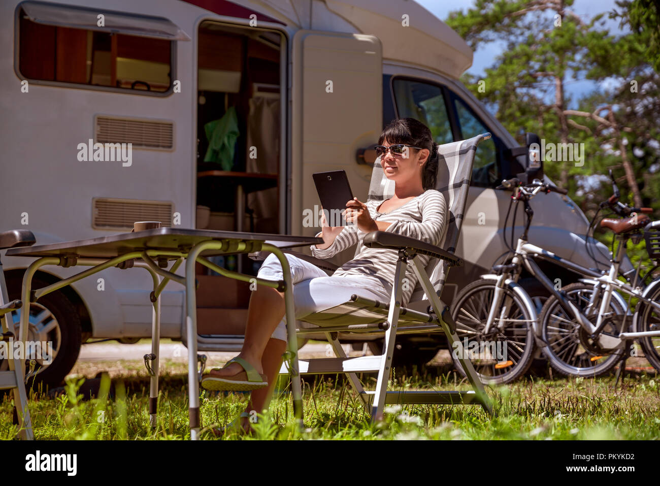 Woman looking at the tablet near the camping . Caravan car Vacation. Family vacation travel, holiday trip in motorhome RV. Wi-fi connection informatio Stock Photo