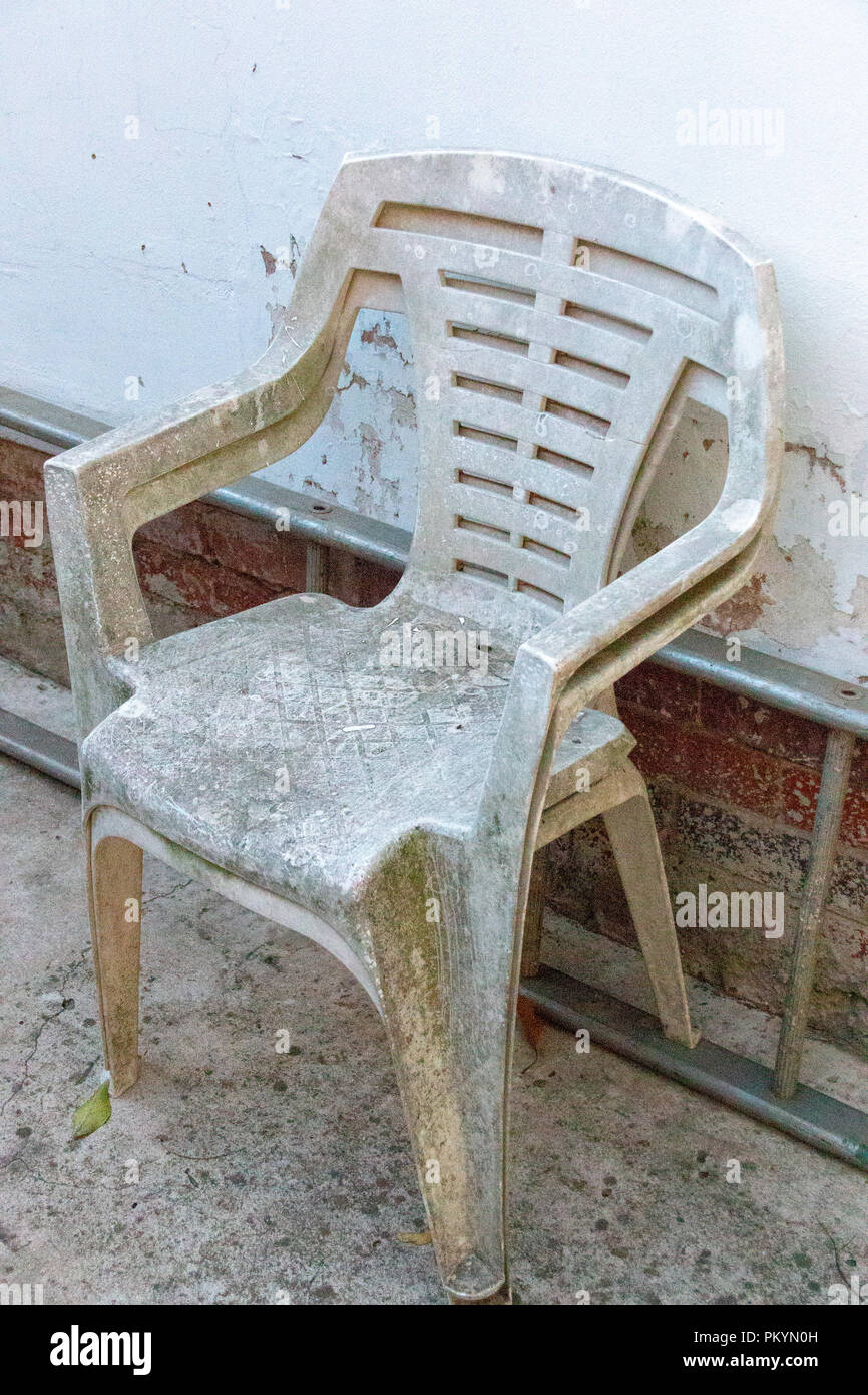 A Close up view of two very old white plastic chairs up against the