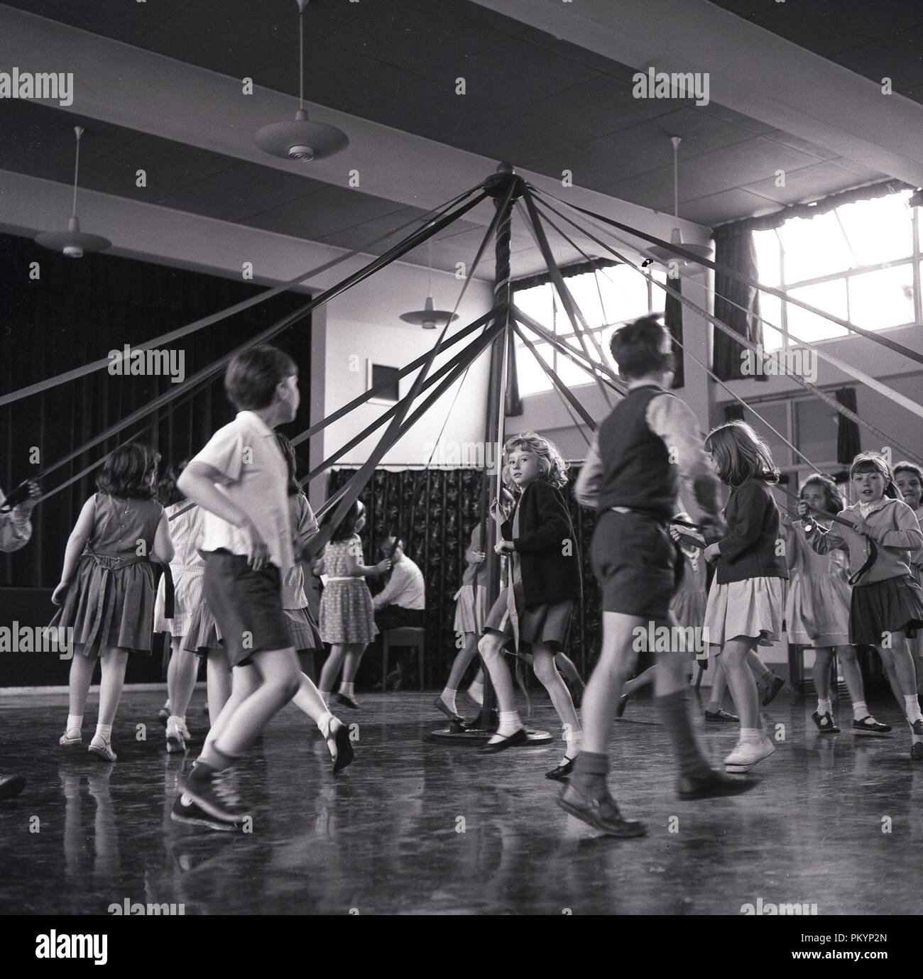 1950s, historical, young school childen skipping or dancing around a maypole inside a hall during a PE class, England, UK. Stock Photo