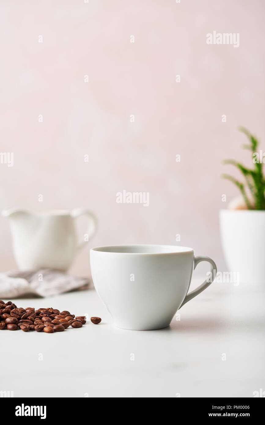 Espresso in a white ceramic coffee cup with roasted coffee beans. Feminine rose background with copy space. Narrow depth of field. Stock Photo