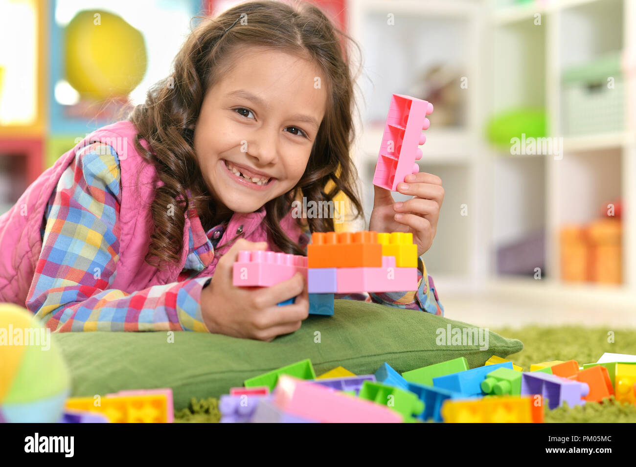 Curly little girl playing with colorful plastic blocks Stock Photo - Alamy