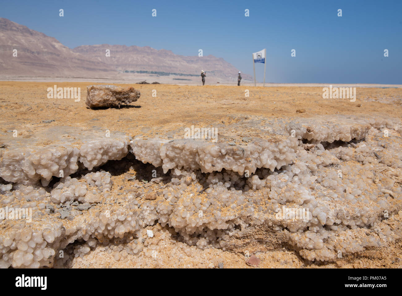 Salt forming on the shore of the sea in Israel with the desert and blurred people behind Stock Photo