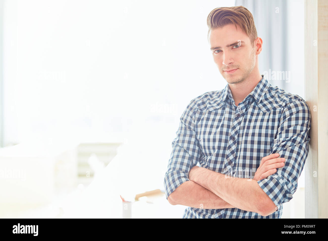 Serious guy with his arms crossed on chest looking at you while leaning