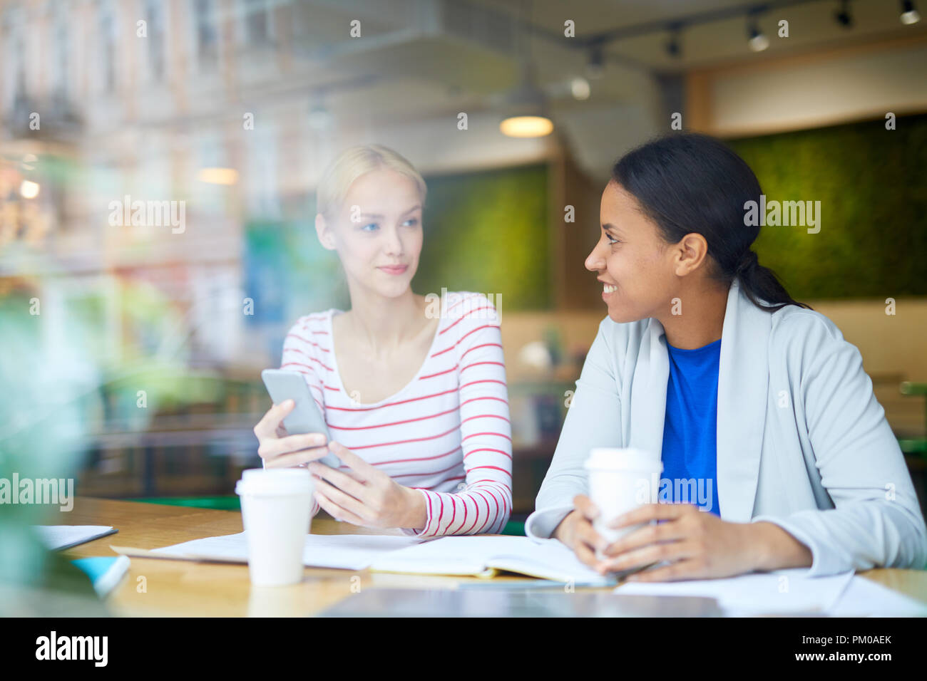 Two intercultural girls in casualwear searching for place to go after work while spending lunch-break in cafe Stock Photo