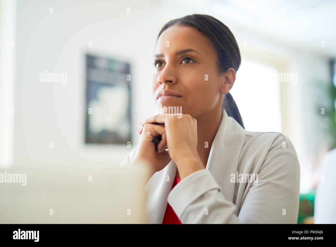 Young pensive mixed-race businesswoman keeping her hands under chin while thinking of something Stock Photo