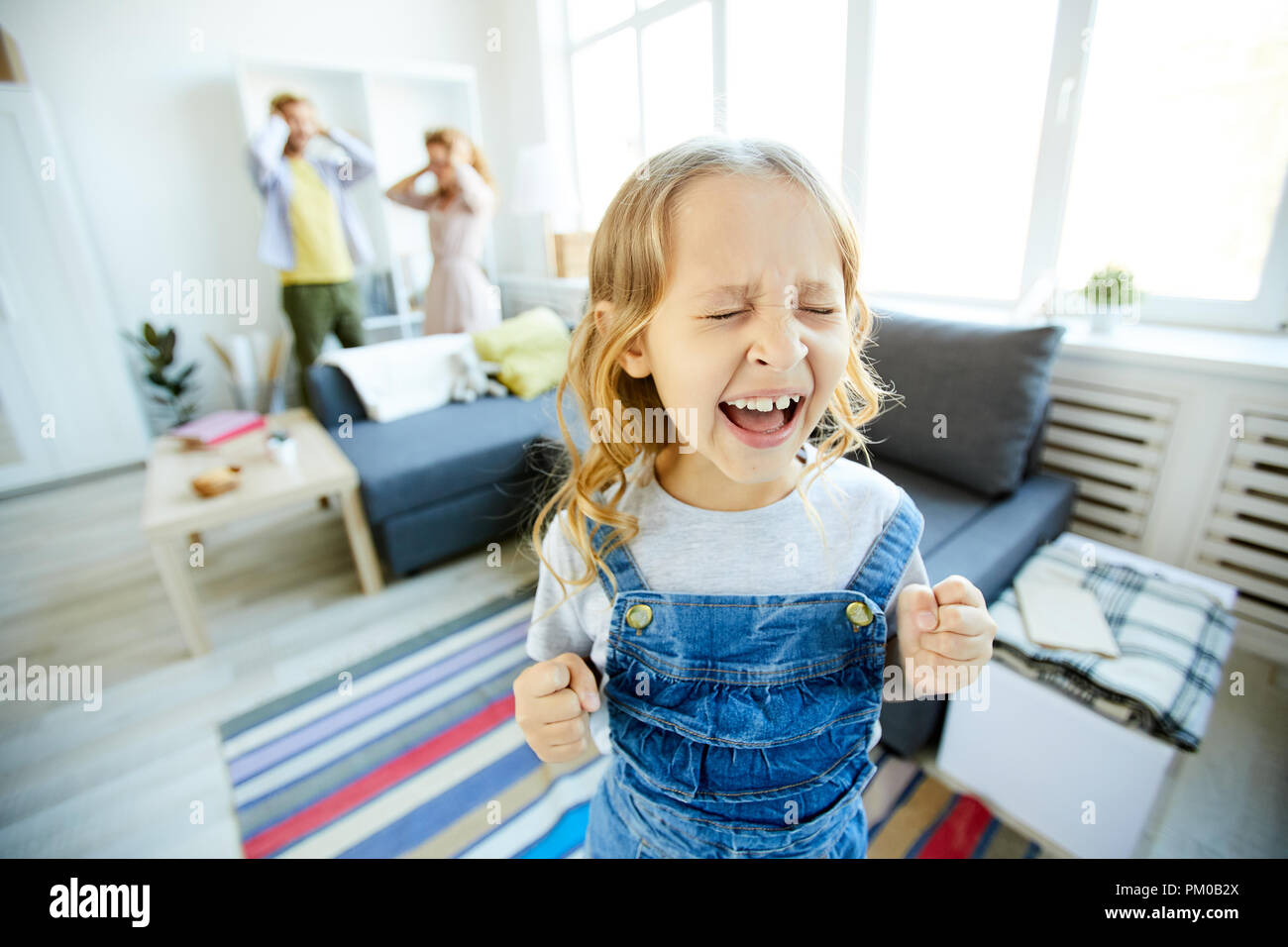 Youthful daughter crying and screaming loudly while being naughty with her shocked parents on background Stock Photo