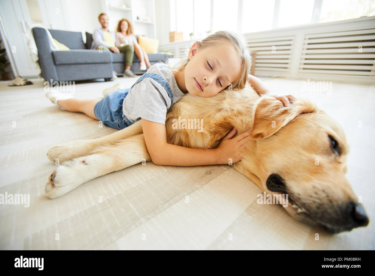 Cute little girl lying on her friendly purebred pet while both relaxing on the floor Stock Photo