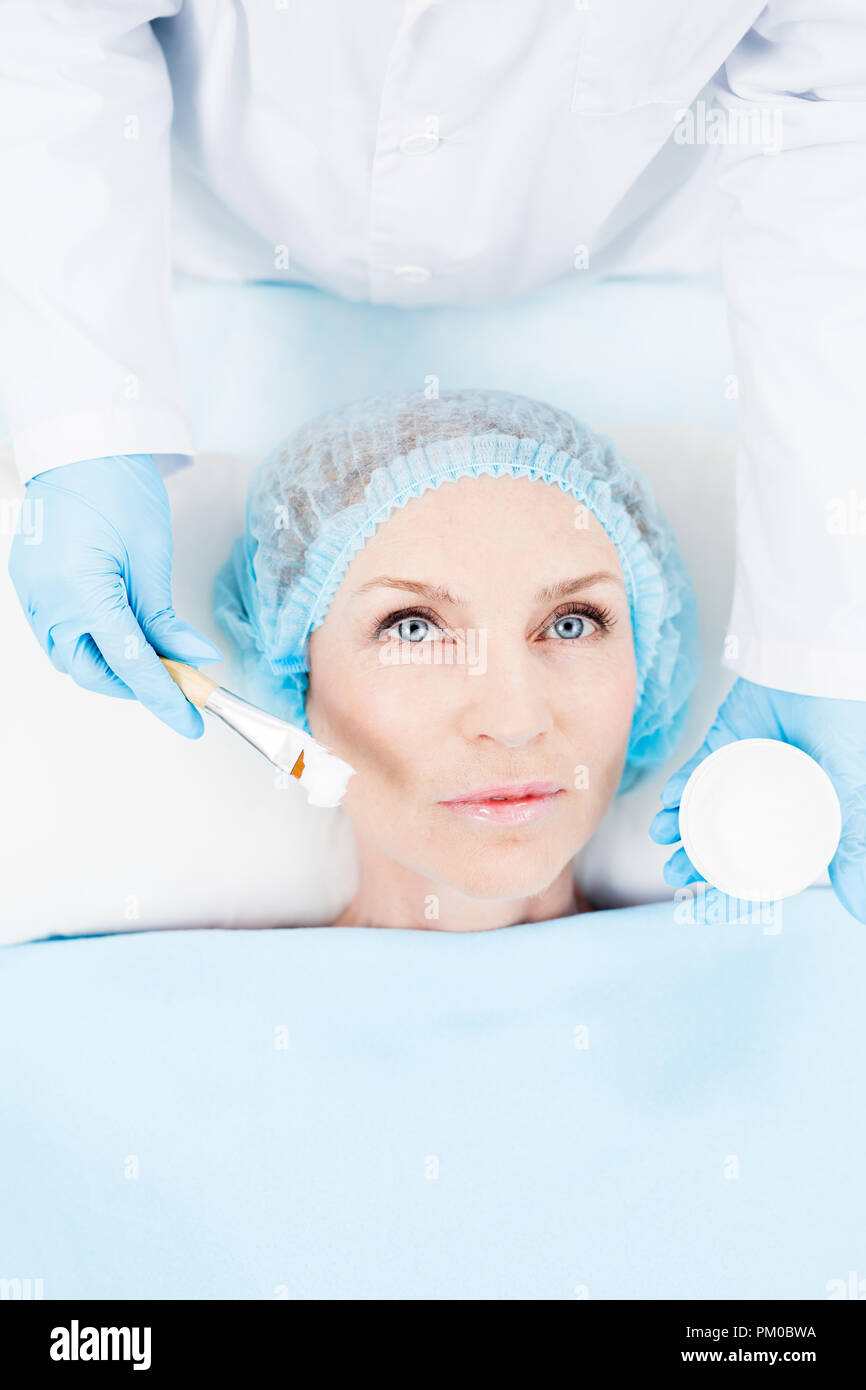 Middle aged woman lying on pillow and having cosmetic procedure on her