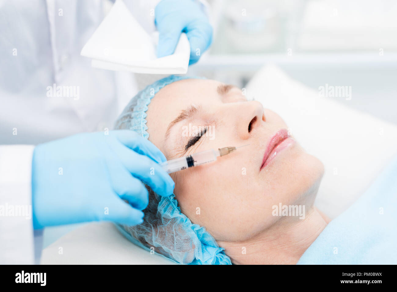 Cosmetician making rejuvenating injection between nose and upper lip of mature client Stock Photo