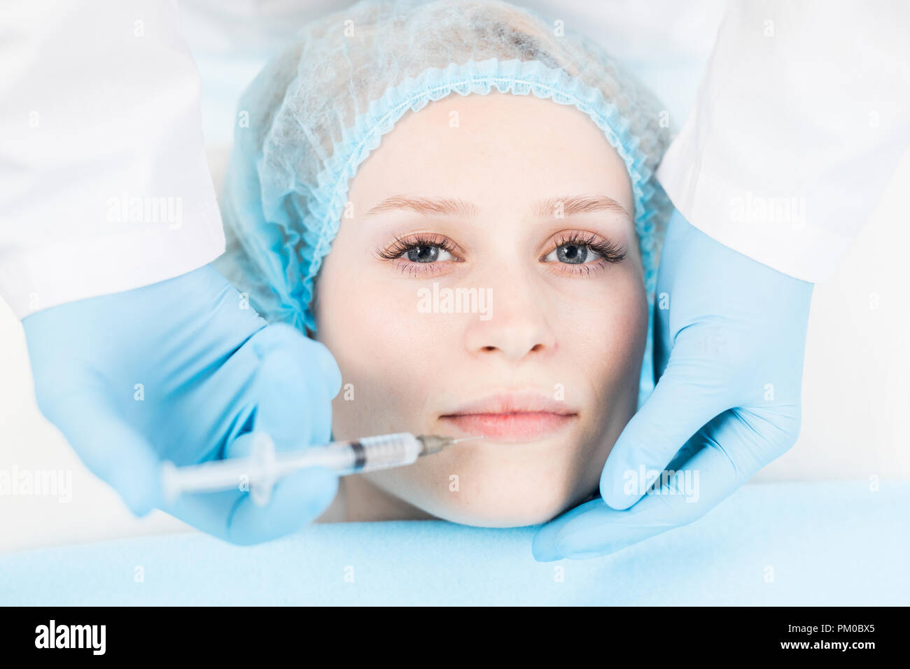 Young woman looking at camera while having lip filler injection in ...