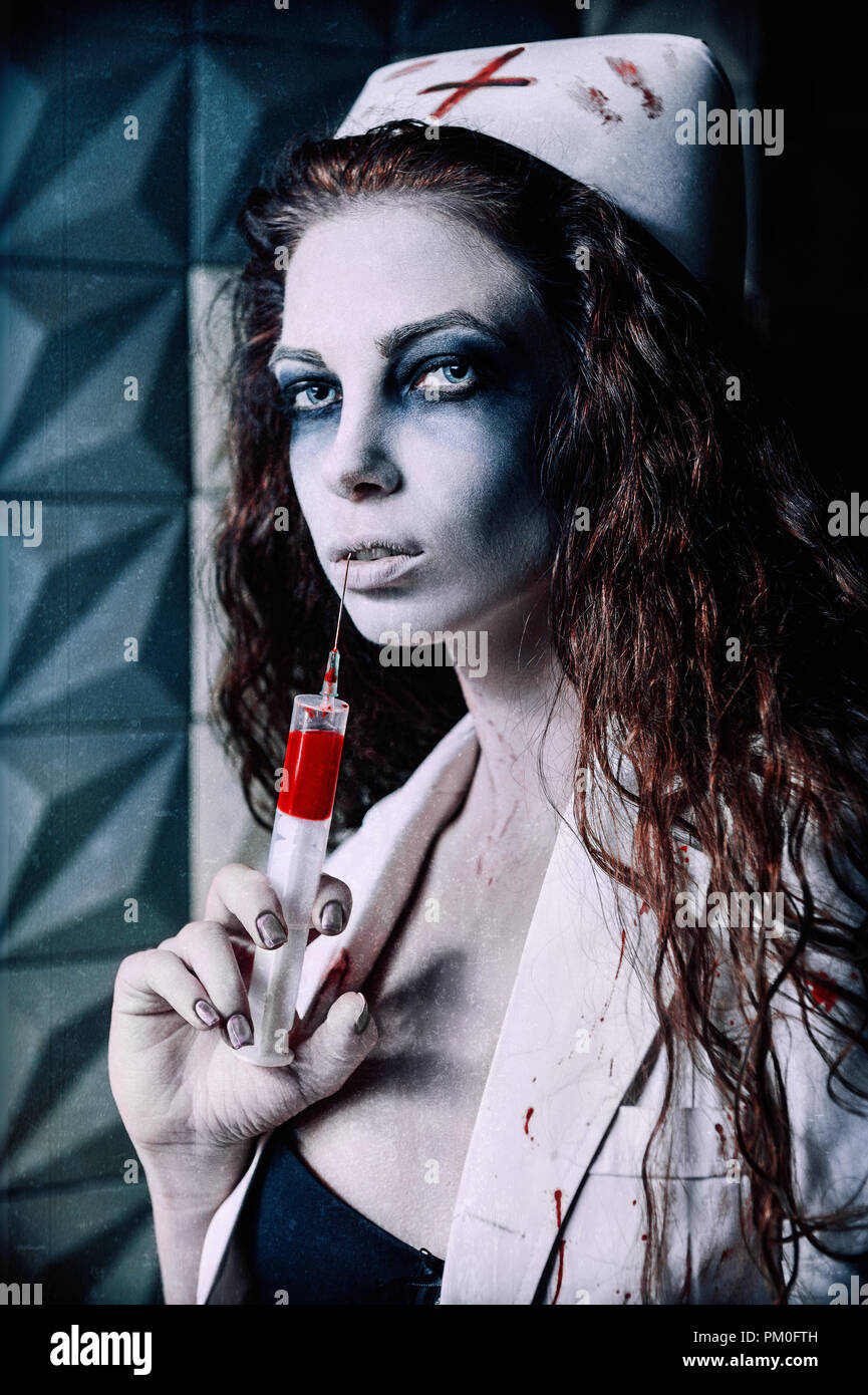 Horror shot: the scary evil nurse (doctor) with bloody syringe in hand. Zombie woman (living dead). Grunge texture effect Stock Photo