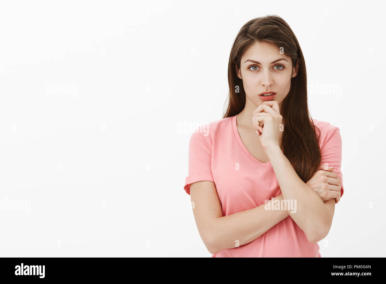 Girl stuck in tough situation, thinking how to solve problem. Portrait of focused intense smart and beautiful woman in pink t-shirt, holding arm crossed and touching chin while gazing strict at camera Stock Photo