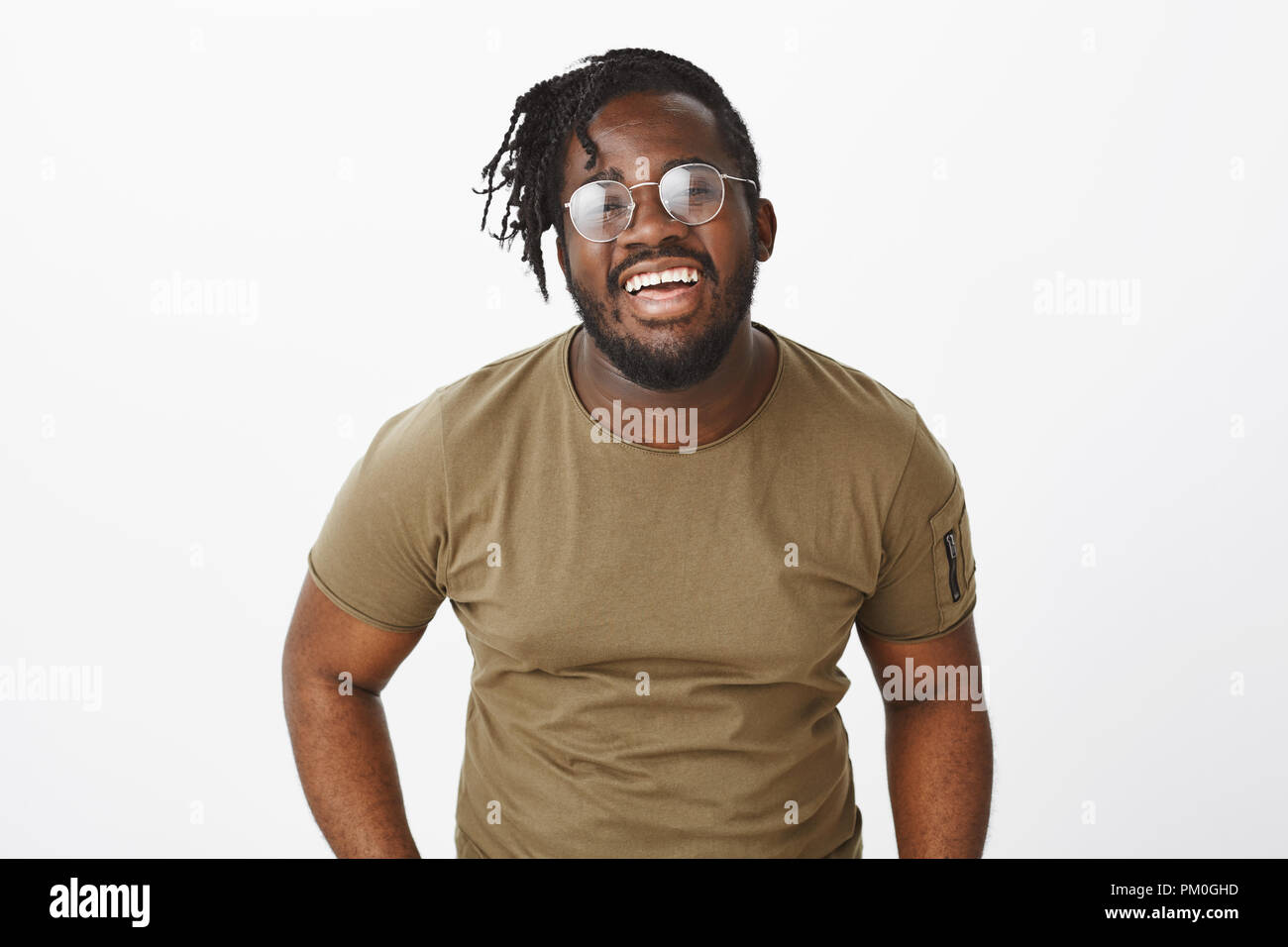 Smile keeps sadness away. Portrait of bright good-looking african american male model in glasses and military t-shirt, laughing out loud and expressing joyful happy attitude over grey wall Stock Photo