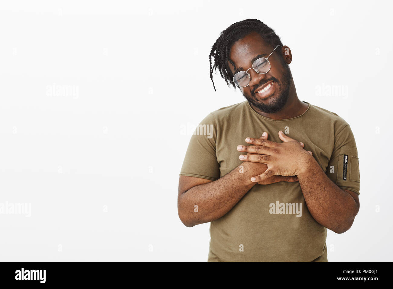 Studio shot of carefree african-american male model in glasses and casual  clothes, holding palms on chest and tilting head with broad smile, being  pleased or touched with warm compliments Stock Photo -
