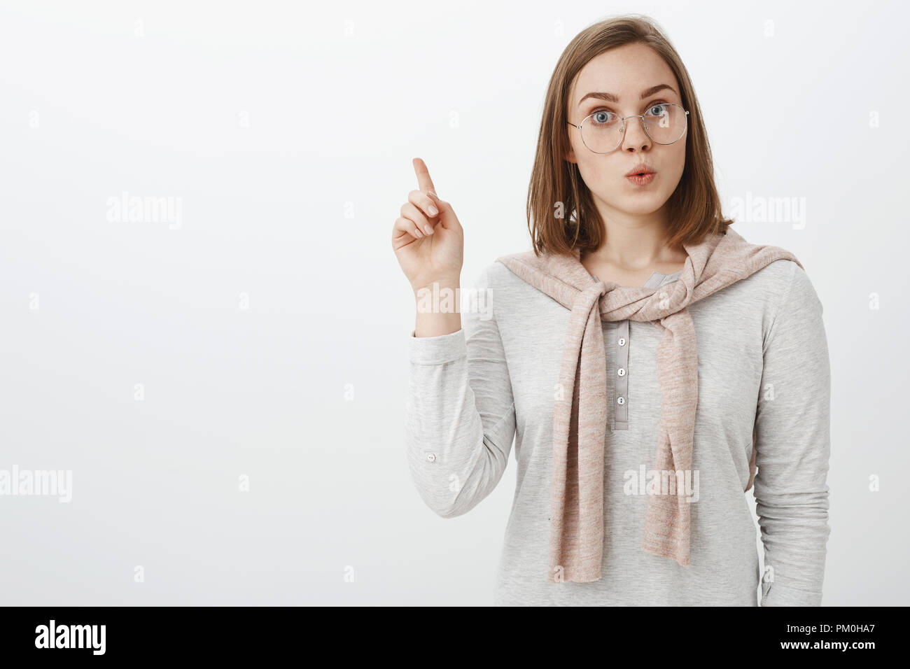 Creative smart excited attractive european female tutor in glasses with pullover tied over neck raising index finger in eureka gesture folding lips with thrill adding interesting suggestion to plan Stock Photo