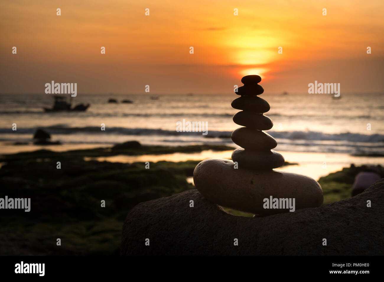 the balanced stack of rocks near the ocean at sunrise. the concept of meditation or strong mind or teamwork spirit Stock Photo