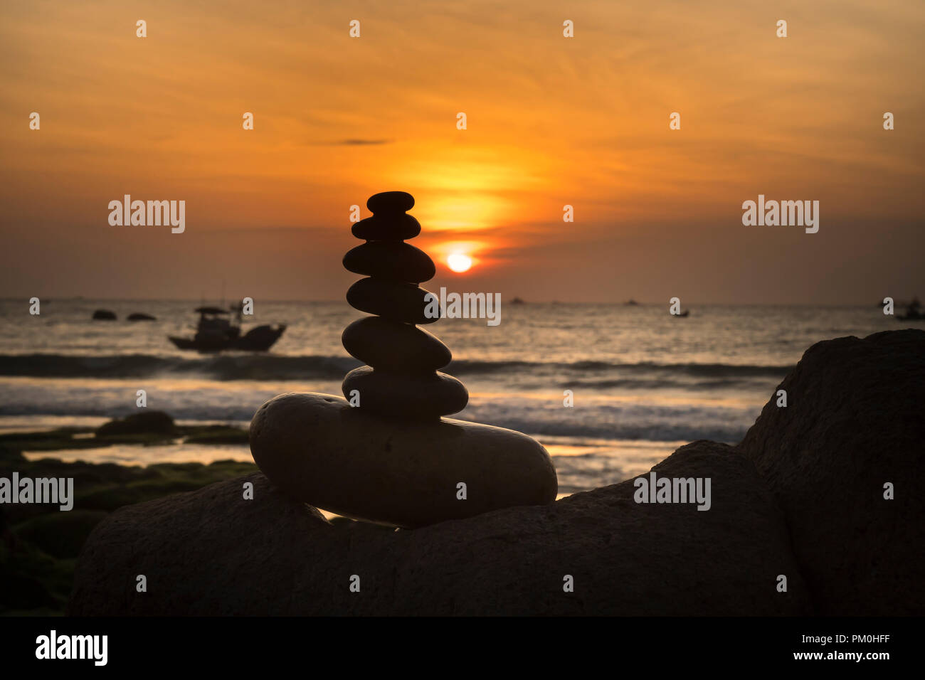 the balanced stack of rocks near the ocean at sunrise. the concept of meditation or strong mind or teamwork spirit Stock Photo