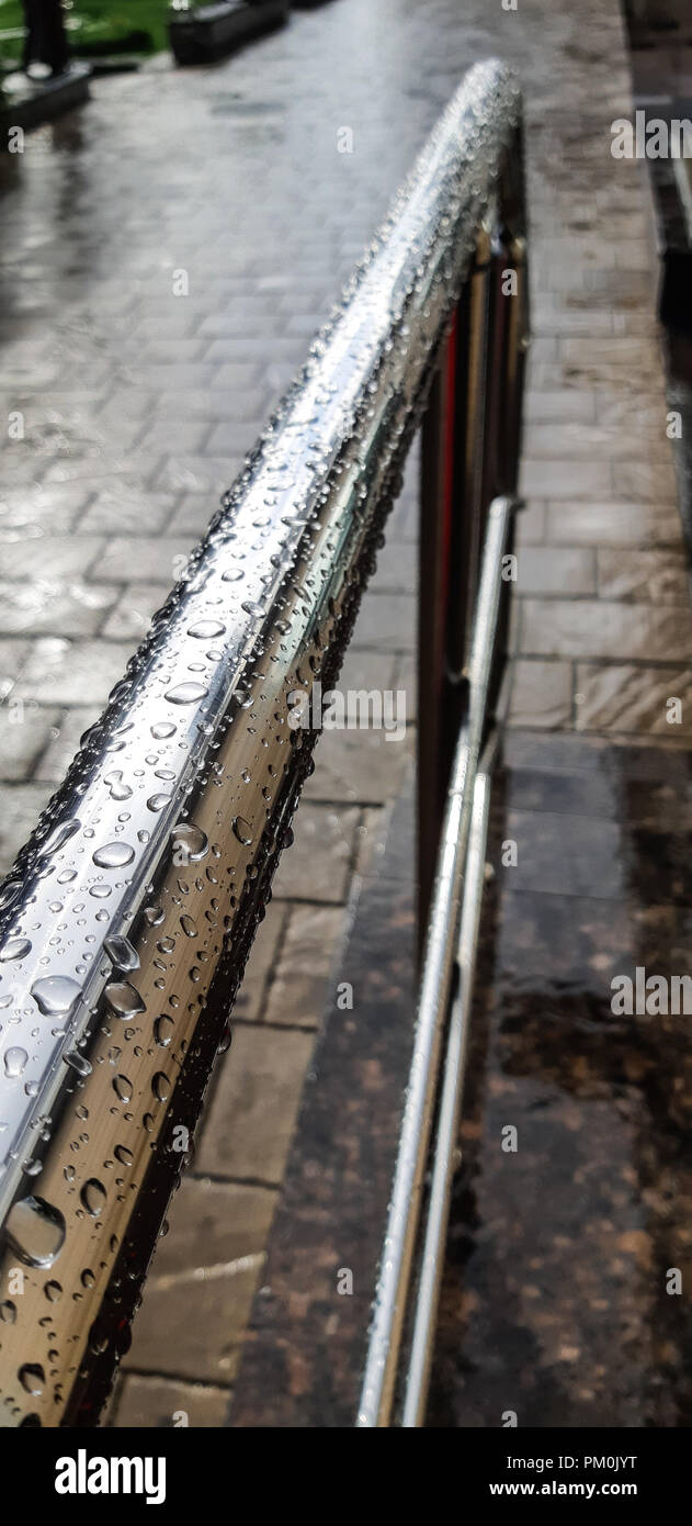 metal chrome-plated handrail in the drops of rain on a cobblestone ...