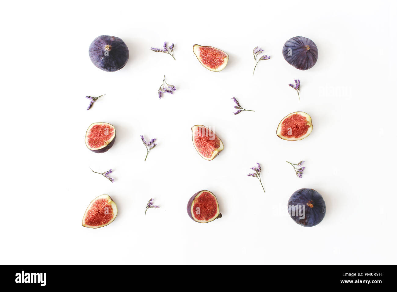 Fresh ripe purple figs. Food Photo. Creative composition of the whole and sliced exotic fruit and violet limonium flowers on a white table background. Floral pattern. Flat lay, view from above. Stock Photo