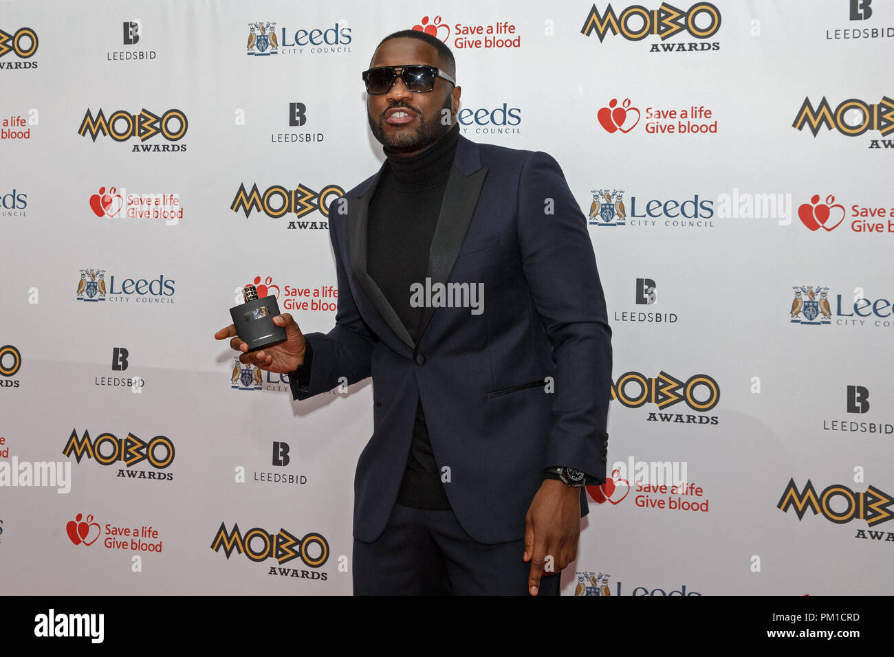 English rapper Lethal Bizzle posing on the red carpet at the 2017 MOBO Awards. The aftershave he is holding is his own brand. He presented at award at the event. Stock Photo