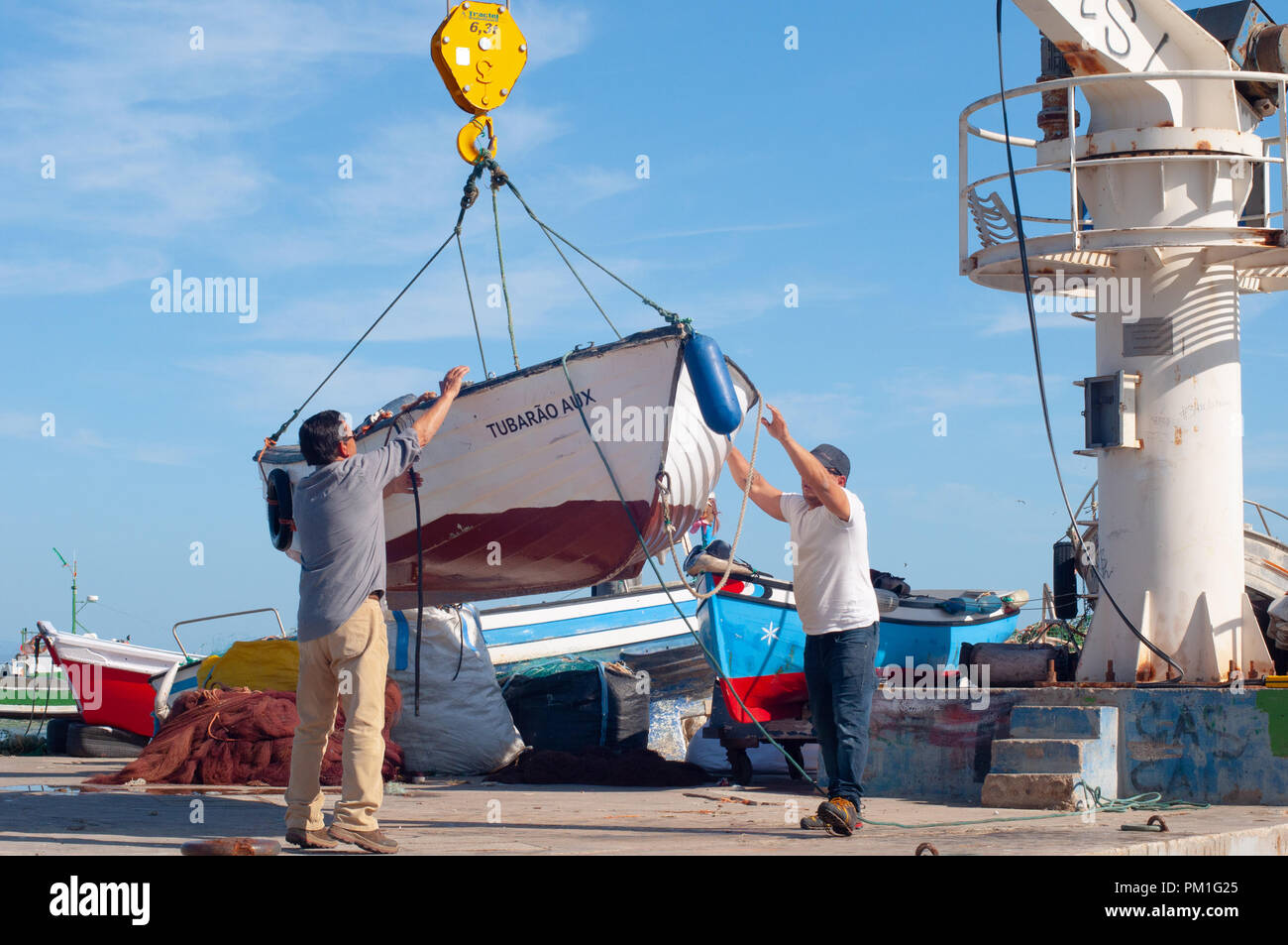 Men Lifting Fishing Boat to Put in Water using Boat Crane Stock Photo