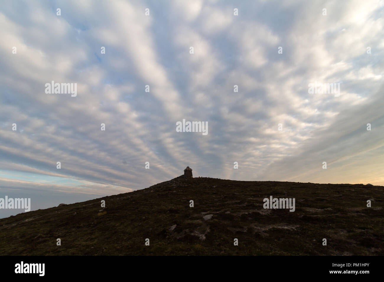 Spectacular evening skyscape over the summit stone shelter of Slieve Meelmore, Mourne Mountains. Stock Photo