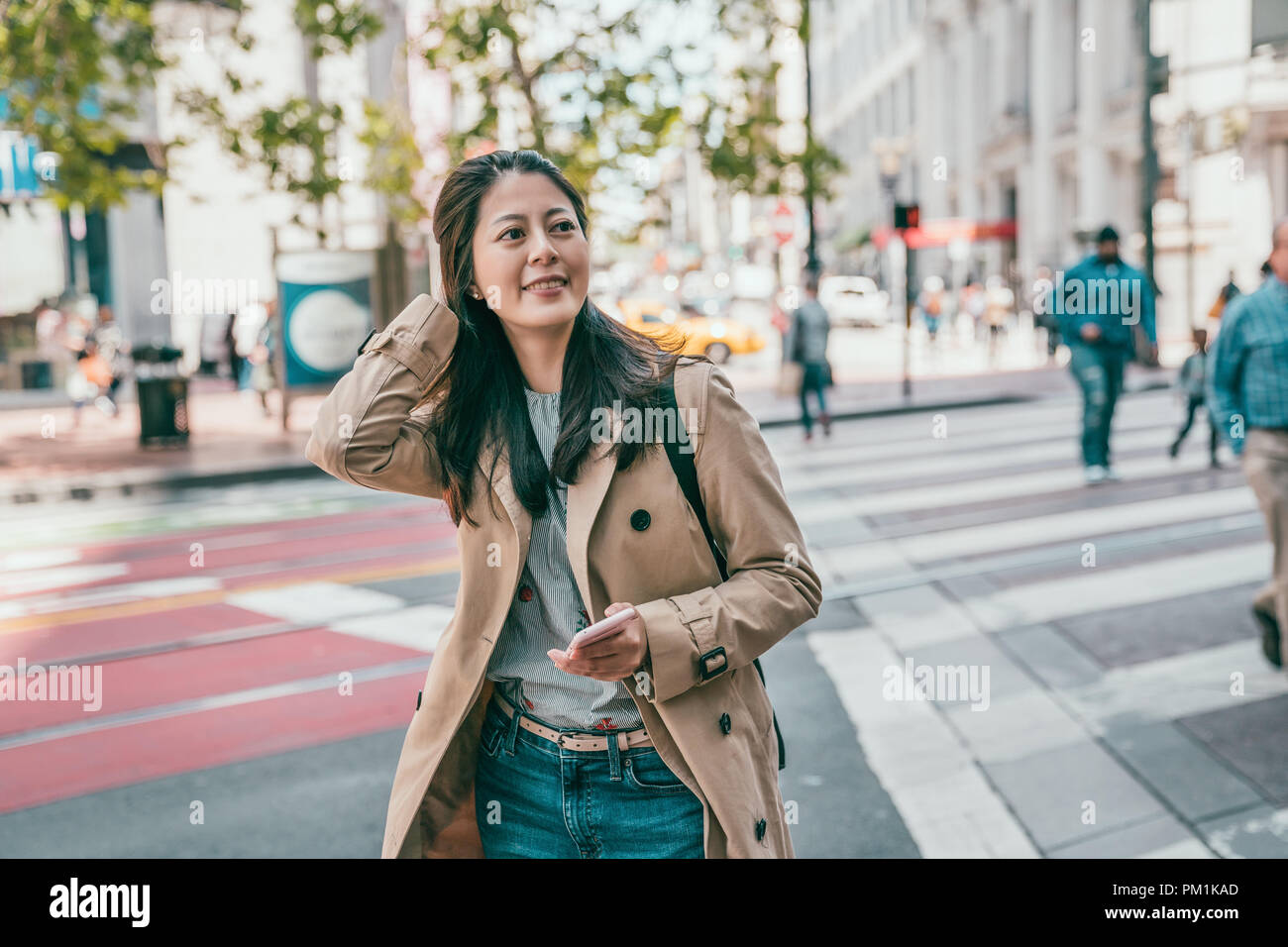 pretty asian international student holding phone and happily crossing the road in san francisco downtown. Stock Photo