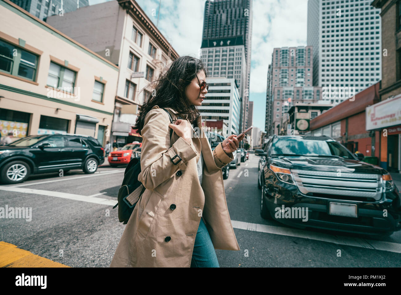 young professional woman crossing the road while using her mobile phone when cars waiting. Stock Photo