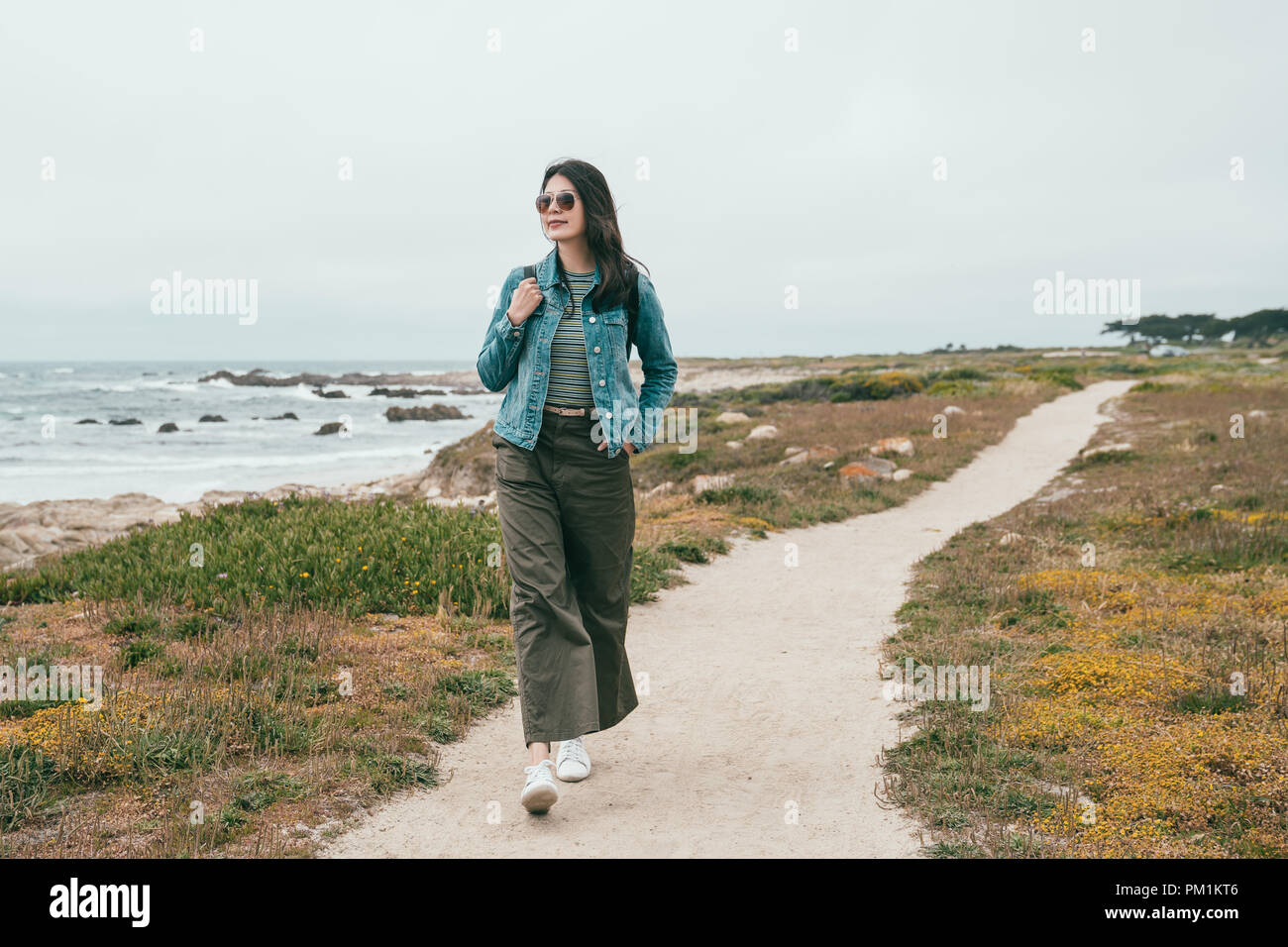 a stylish travel woman walking in a beach path and feeling satisfied by this peaceful place. Stock Photo