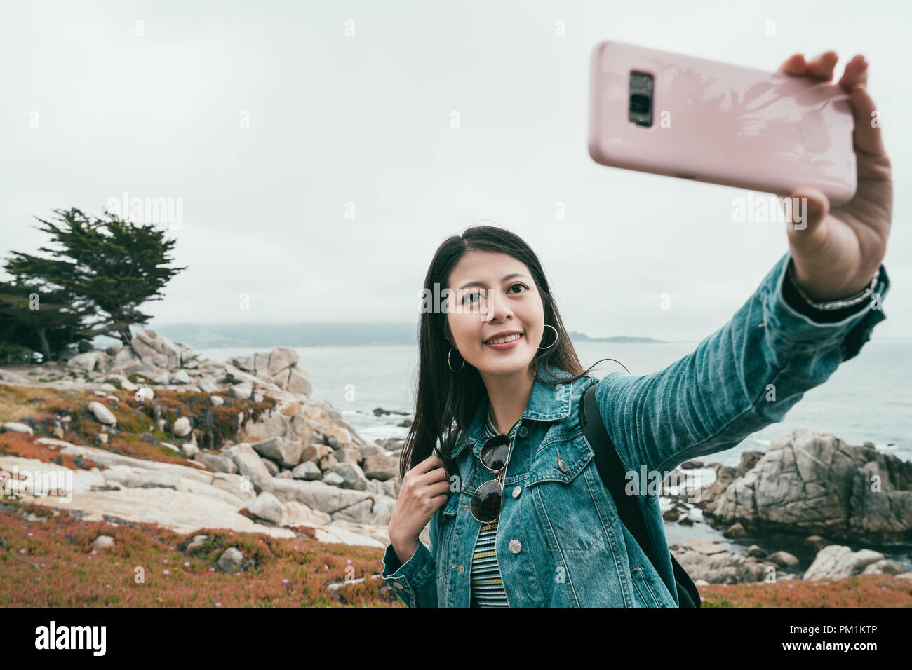 young lovely woman taking selfies at the beach by her cell phone in a small and quiet town. Stock Photo