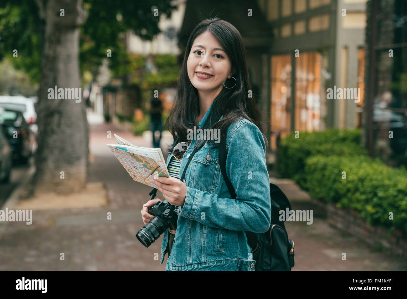 woman smiling joyfully to the camera and holding a guide map in hands while walking sightseeing. Stock Photo