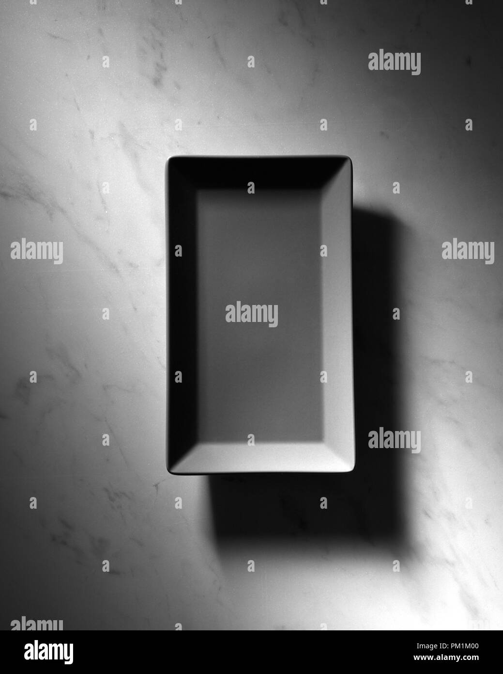 Black rectangular empty plate presented on a gray marble background with shadows, space for text. Top view Stock Photo