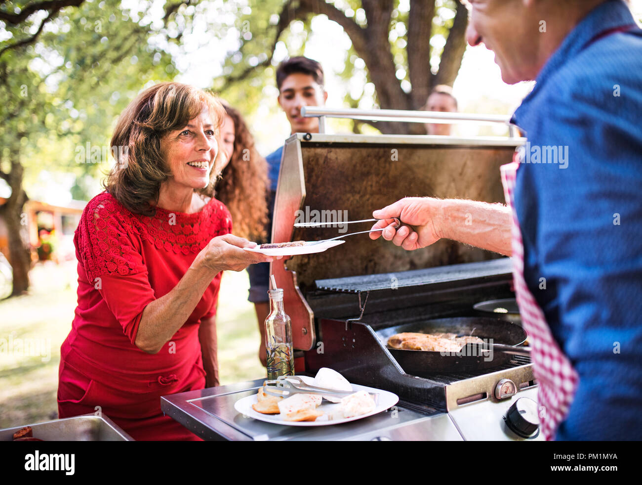 A senior man with family and friends cooking food on a barbecue on a ...