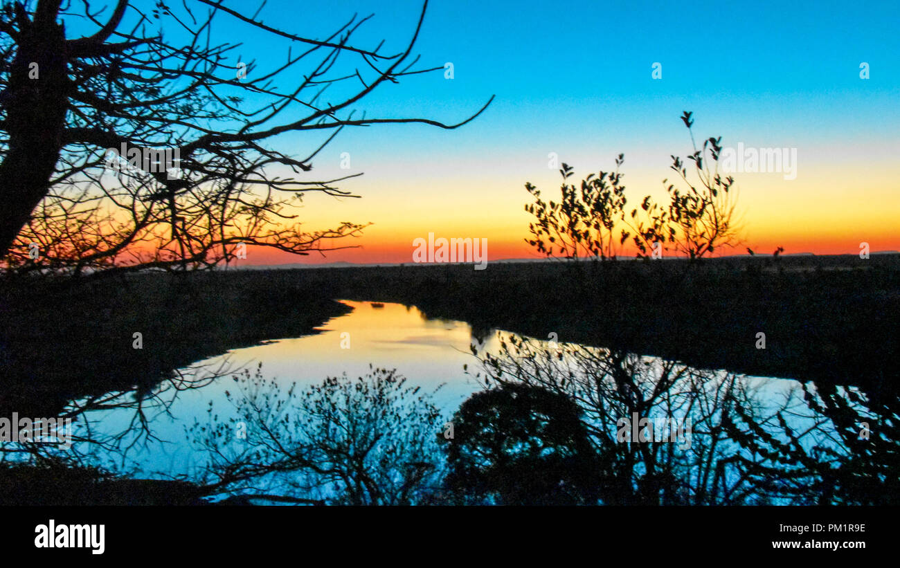 Serene sunset landscape with river in the foreground and golden skies at sunset. A serene setting ideal to enjoy a sun downer under African skies Stock Photo