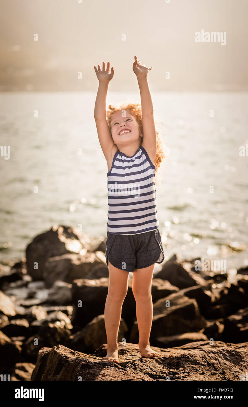 Little girl with with raised hands on a rock near a sea Stock Photo - Alamy